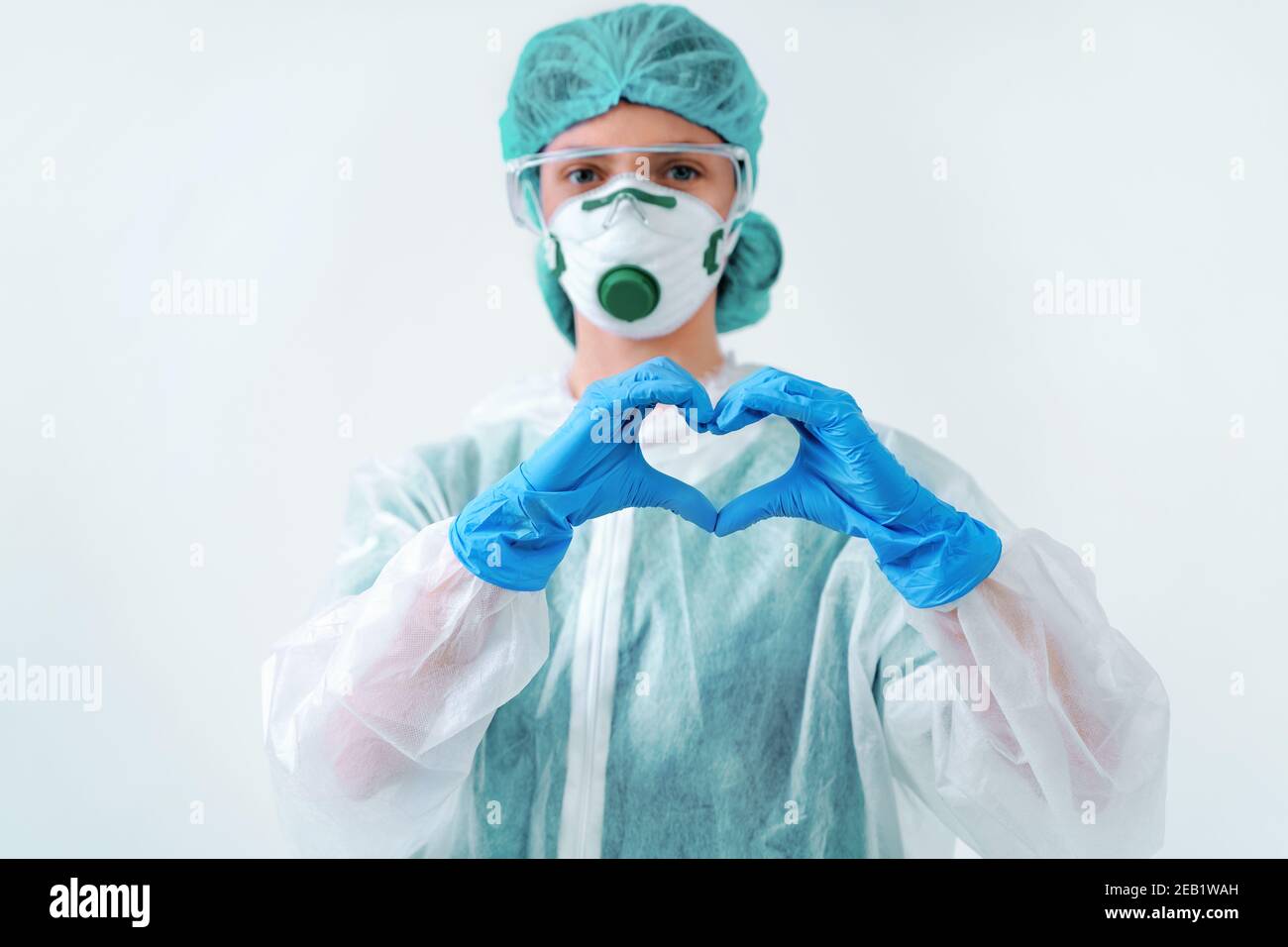 Operatore sanitario in tuta protettiva e maschera medica che fa forme cuore con entrambe le mani Foto Stock