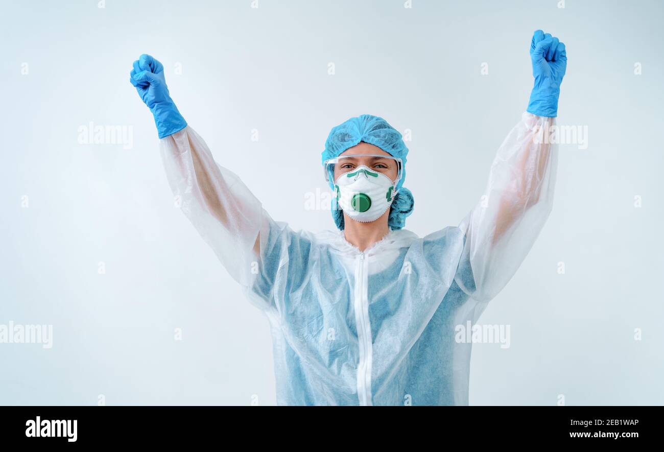 Operaio sanitario in tuta protettiva e maschera medica clenches pugni in gesto di vittoria, esclamato con felicità. Foto Stock