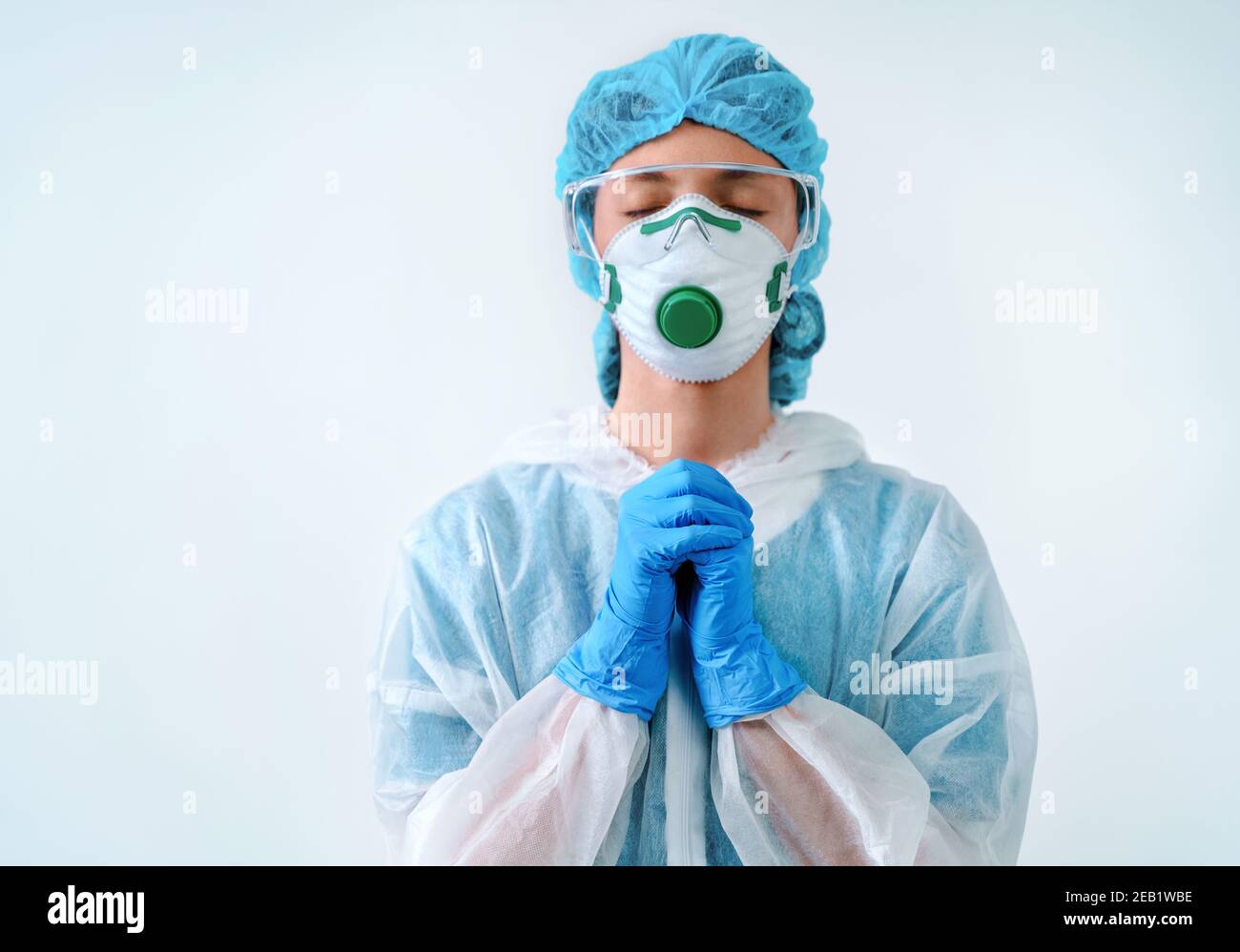Operatore sanitario in tuta protettiva e maschera medica mettendo le mani insieme nella preghiera Foto Stock