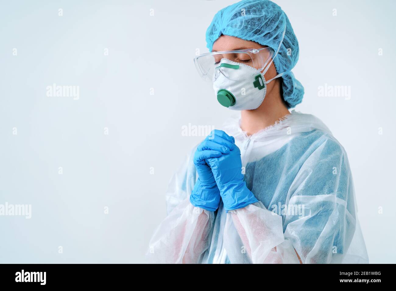 Operatore sanitario in tuta protettiva e maschera medica mettendo le mani insieme nella preghiera Foto Stock