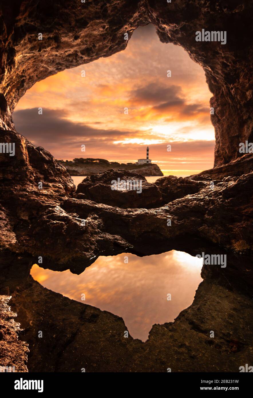 Faro di Portocolom, Maiorca, visto dall'interno di una grotta all'alba con una pozza in primo piano che riflette il cielo Foto Stock