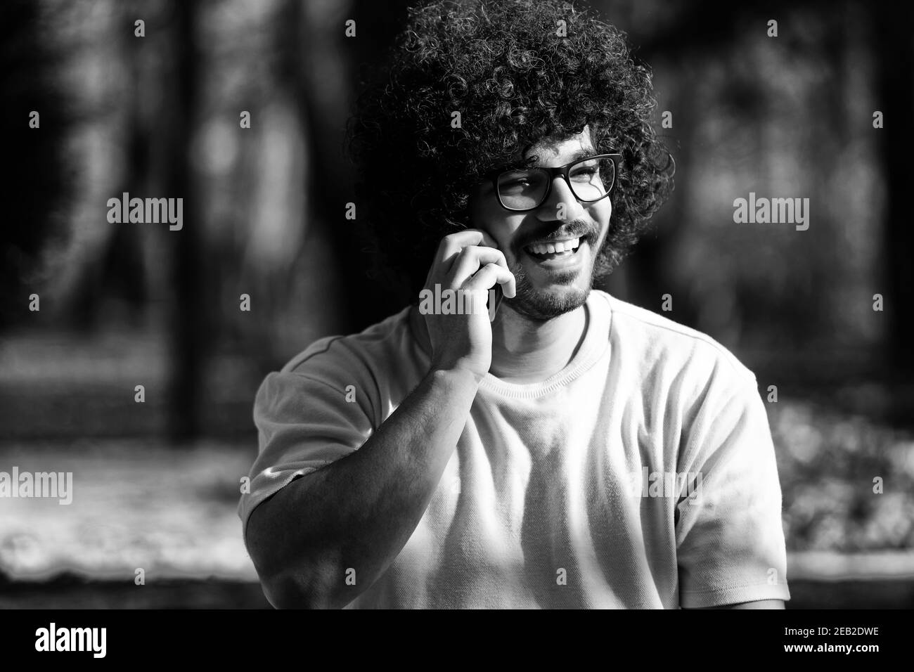 Ritratto di bel giovane Afro uomo che parla sul cellulare Telefono e seduta fuori durante l'autunno Foto Stock