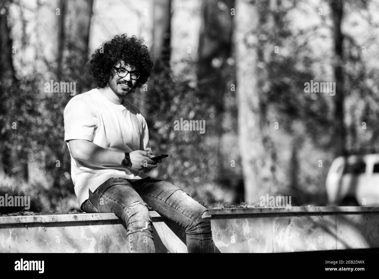Ritratto di bel giovane afro uomo che parla toccando Telefono o. Utilizzo dello smartphone per la chiamata e la presenza all'esterno durante l'autunno Foto Stock