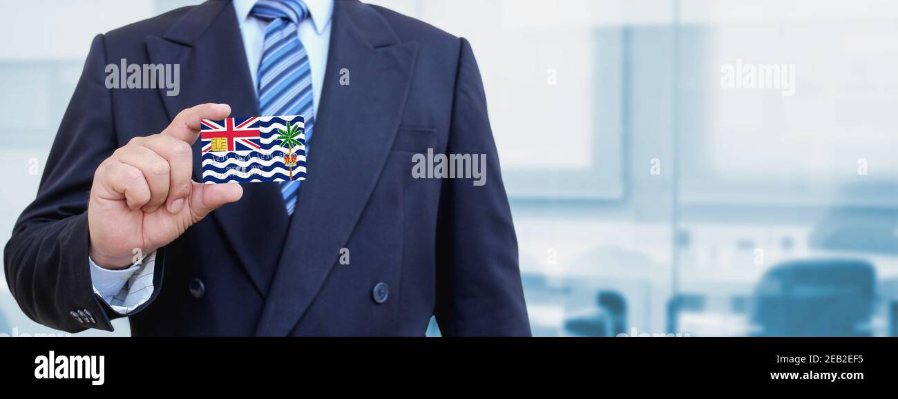 Immagine ritagliata di un uomo d'affari che detiene carta di credito in plastica con bandiera stampata dell'Oceano Indiano britannico. Sfondo sfocato. Foto Stock
