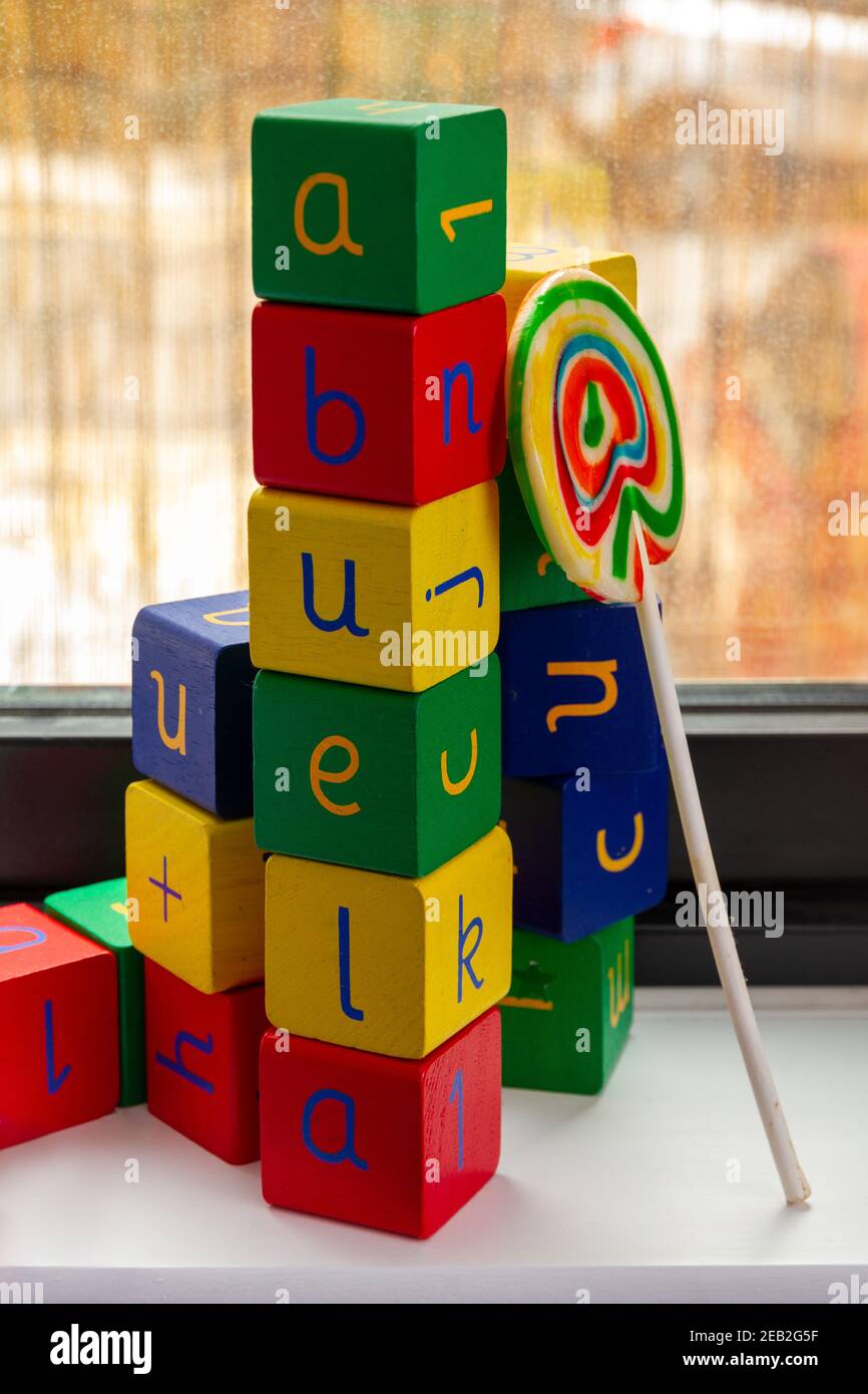 Una torre di colorati blocchi di giocattoli in legno con lettere e. numeri che formano la parola 'abuela' (nonna) con un lollipop da una finestra Foto Stock