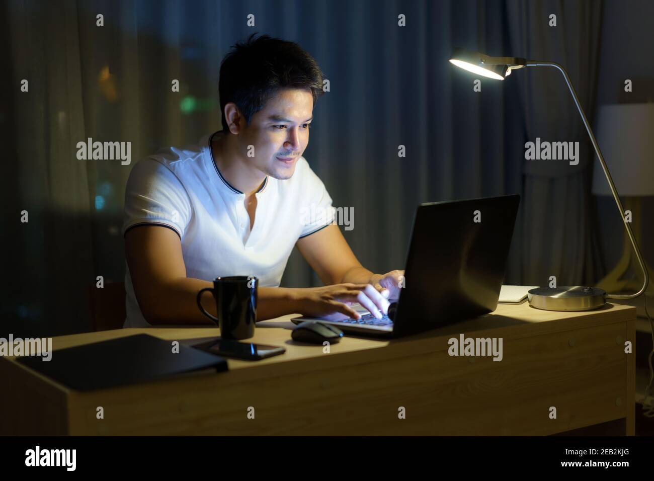 L'uomo asiatico che lavora a casa è seduto di fronte a un computer a tarda notte. Foto Stock