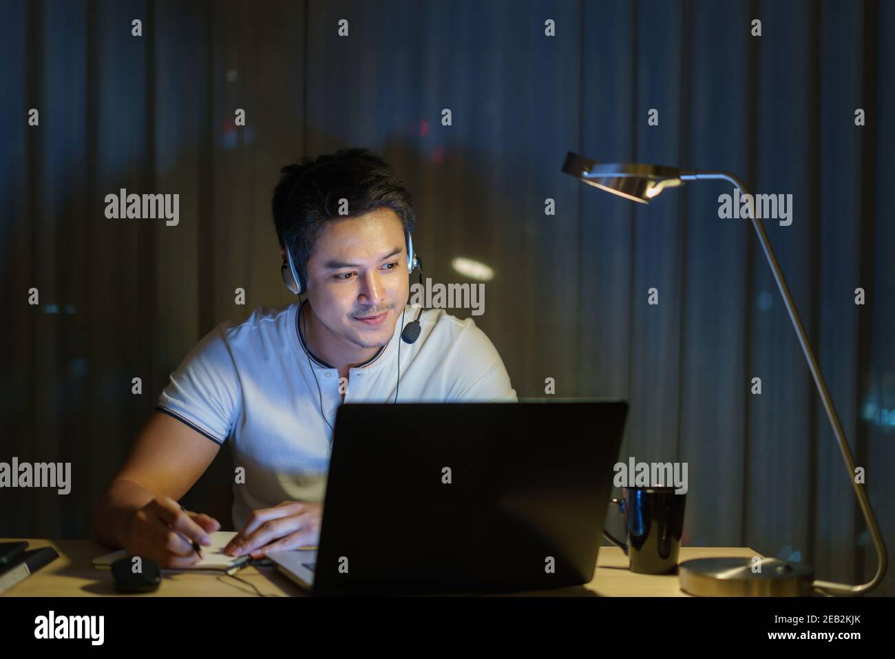 L'uomo asiatico lavora a casa è seduto al lavoro con colleghi o manager tramite videochiamata di notte a casa. Foto Stock