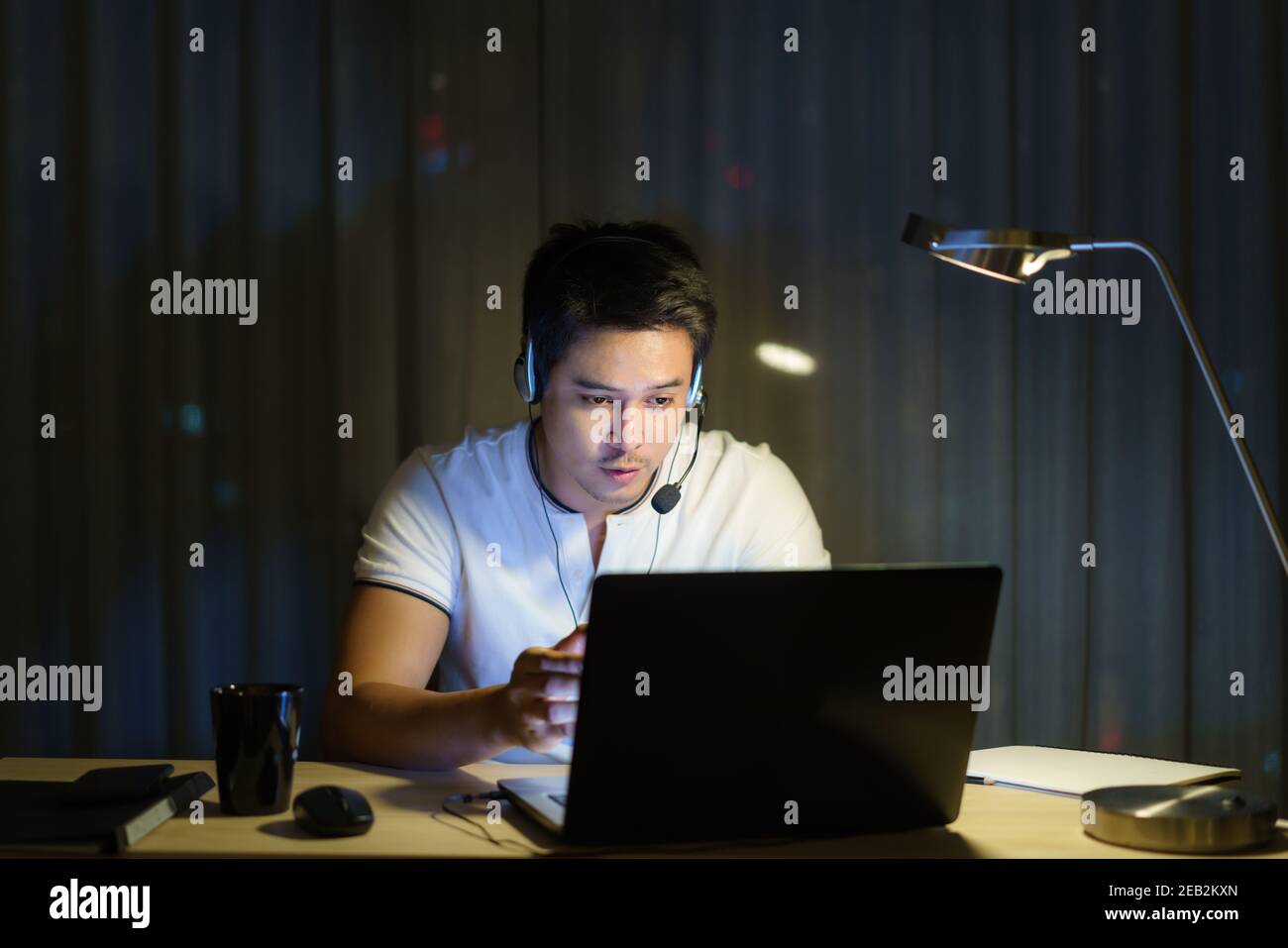 L'uomo asiatico lavora a casa è seduto al lavoro con colleghi o manager tramite videochiamata di notte a casa. Foto Stock