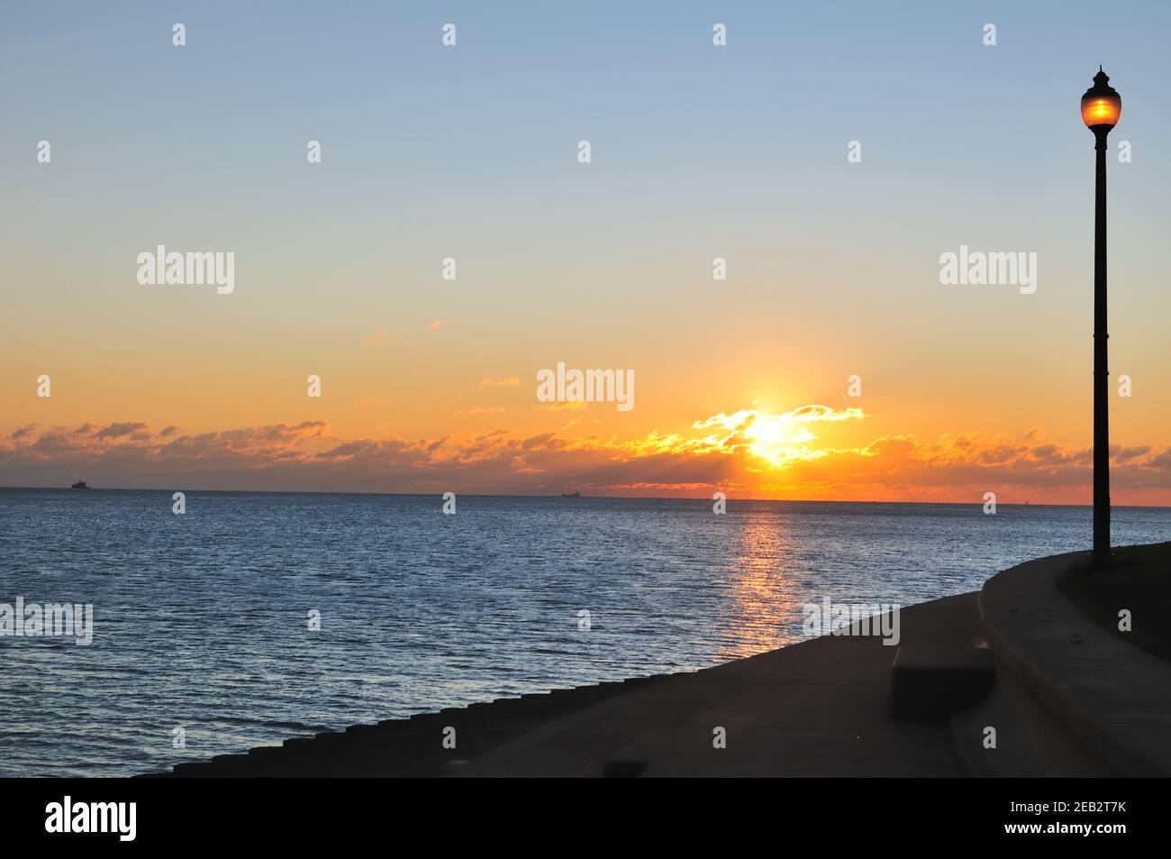 Chicago, Illinois, Stati Uniti. Il sole sorge dietro le nuvole all'orizzonte, come il suo bagliore corrisponde alla luce di strada che fiacca la passeggiata del lago. Foto Stock