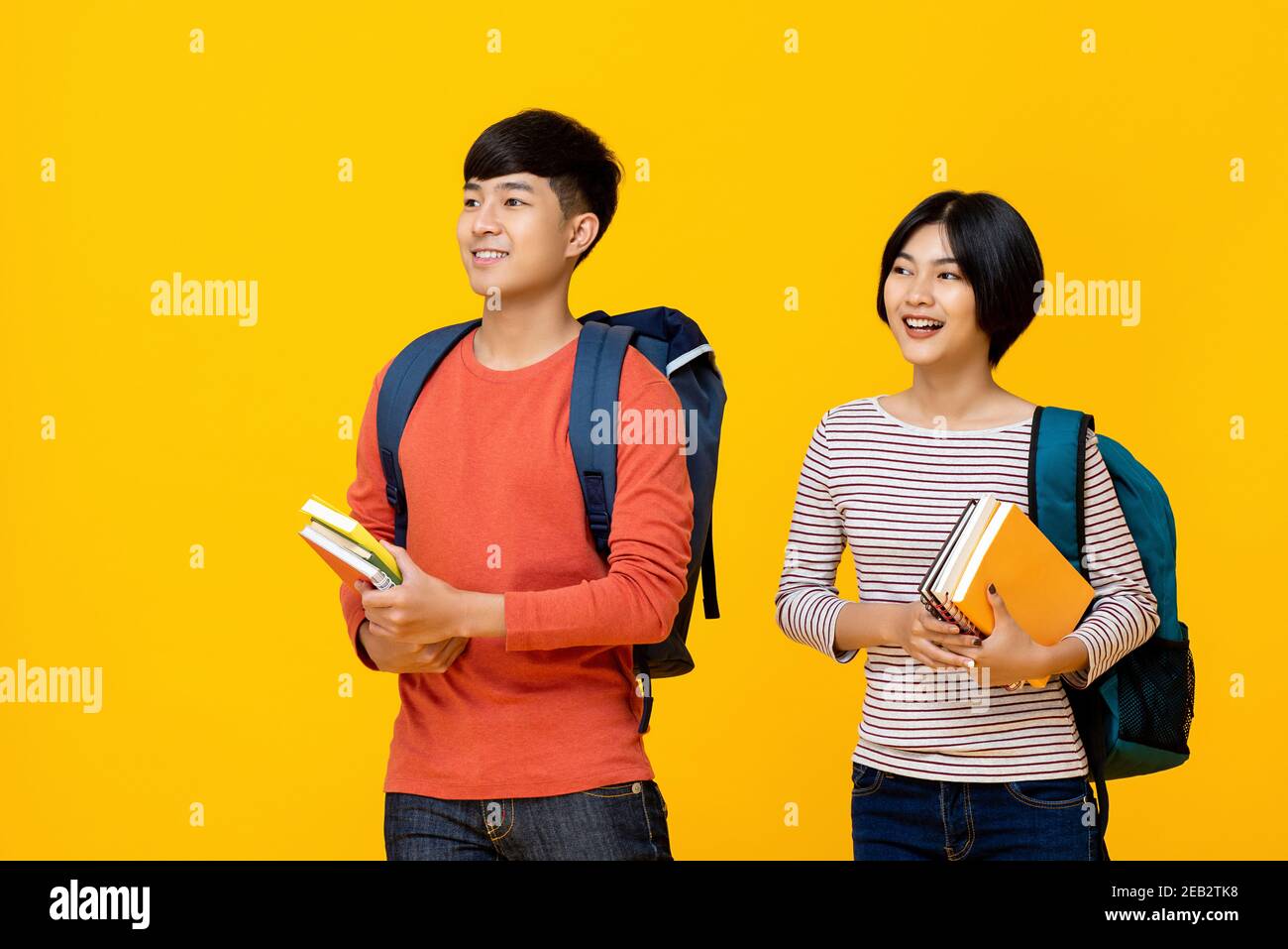 Felice sorridente giovani studenti asiatici che portano libri a scuola sfondo di studio isolato giallo Foto Stock