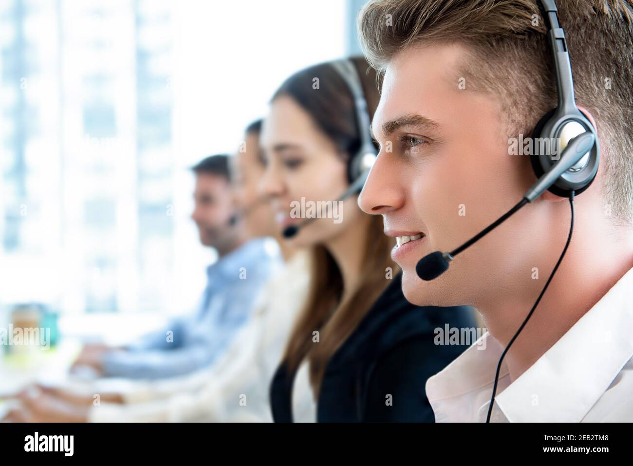 Uomo sorridente e cordiale che lavora in ufficio presso il call center con il team come agenti di telemarketing del servizio clienti Foto Stock