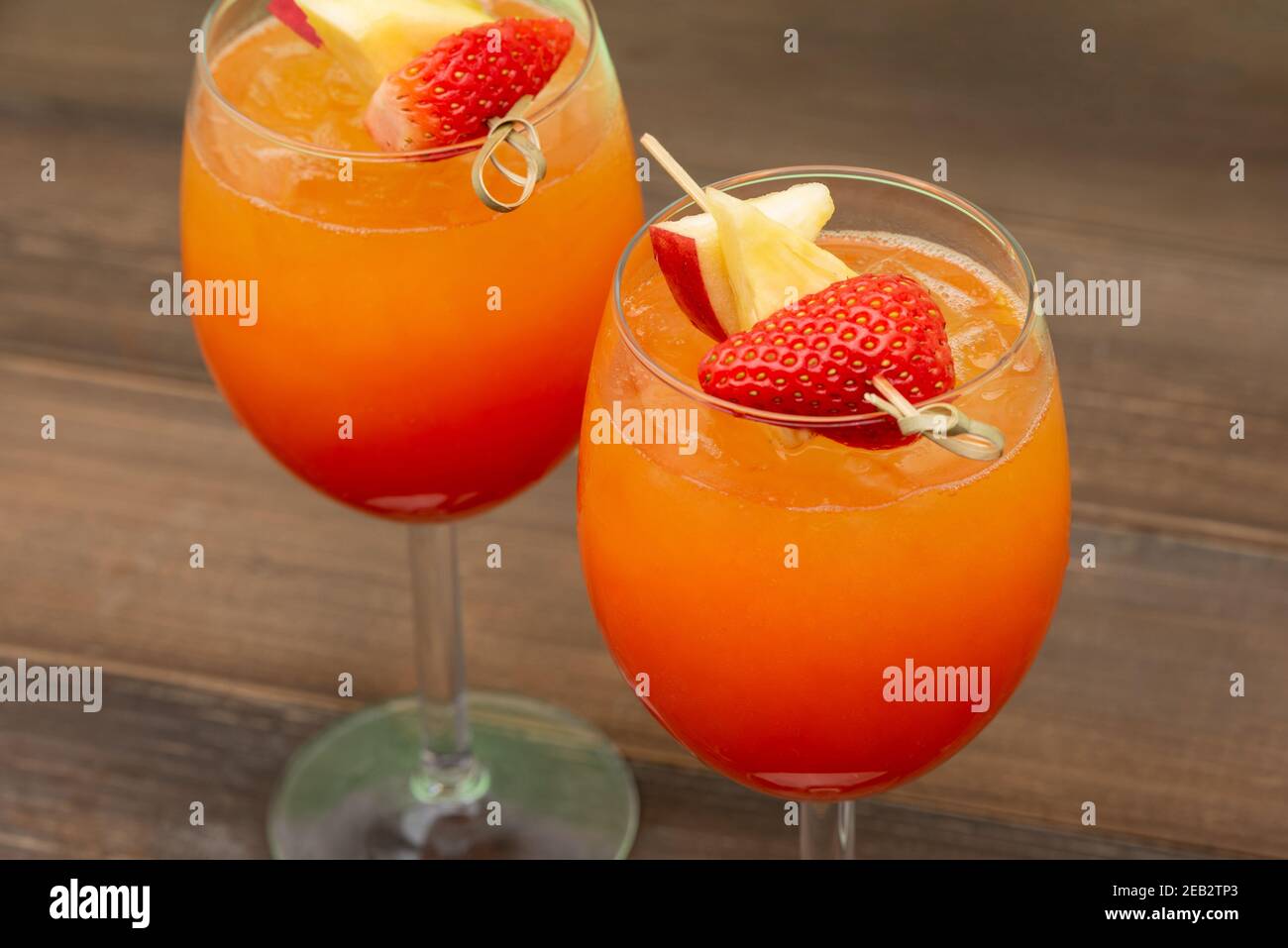 Cocktail colorati e rinfrescanti all'alba con fragola e arancio nei bicchieri su sfondo tavola di legno Foto Stock