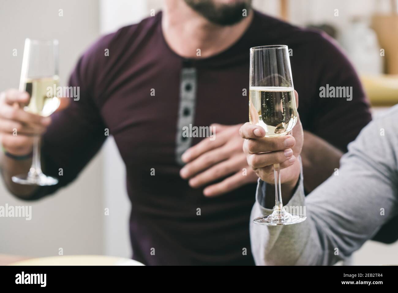 Due mani maschili che tengono in mano bicchieri di vino bianco frizzante riunione sociale Foto Stock