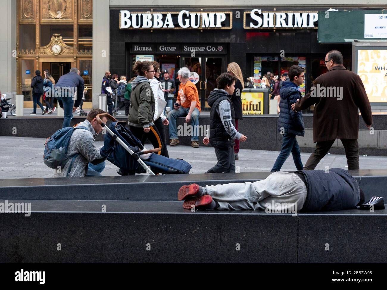 Un uomo dorme in Times Square mentre i turisti camminano. Foto Stock