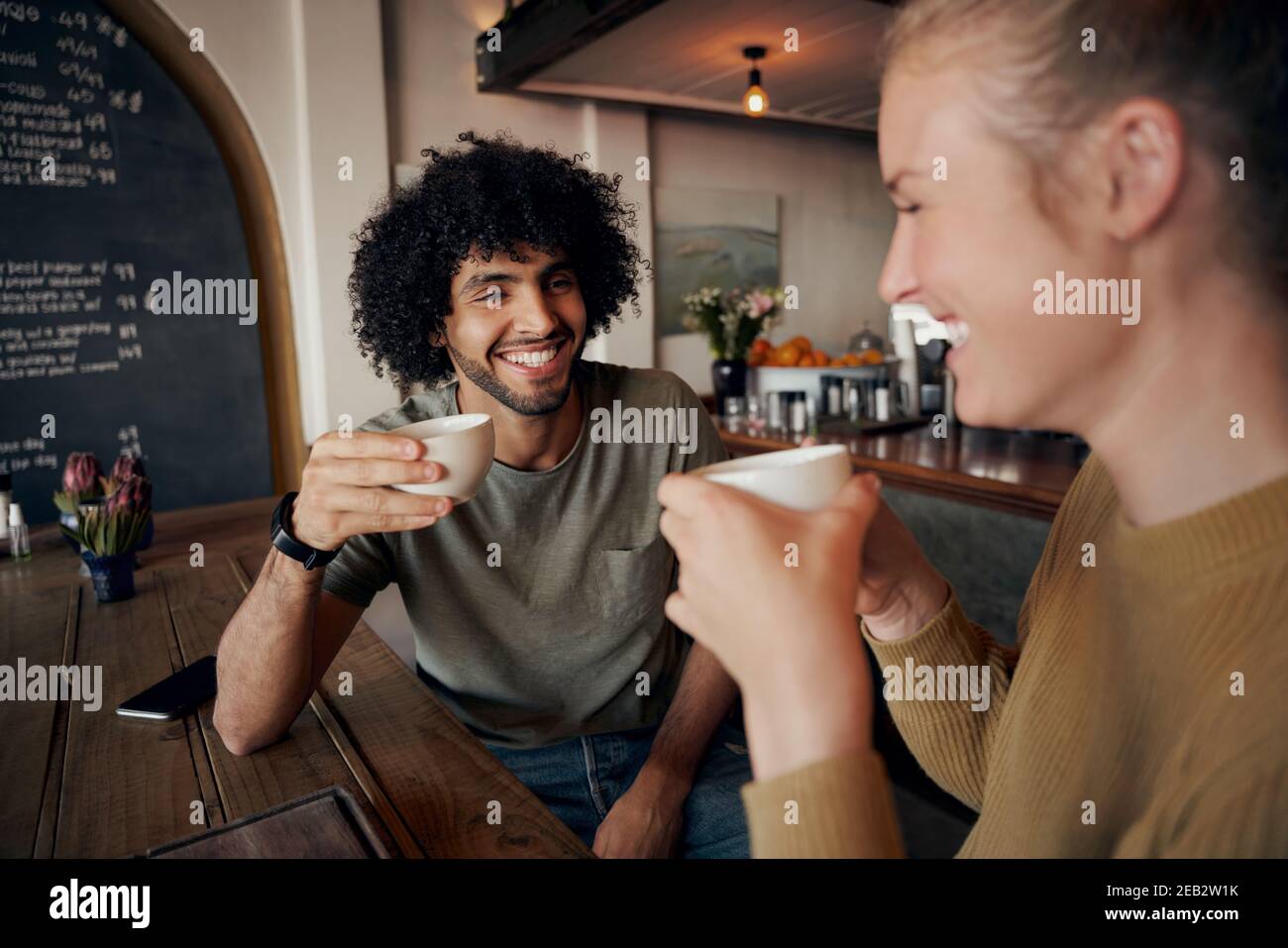 Giovane coppia allegra che si gode la data mentre parla e ride dentro caffè moderno e caffè appena preparato Foto Stock