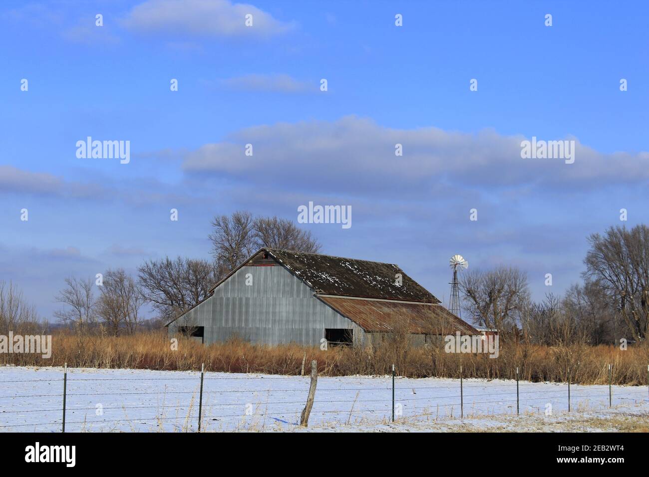 Kansas Country Barn con neve, recinzione, cielo blu e nuvole nel paese che è luminoso e colorato. Foto Stock
