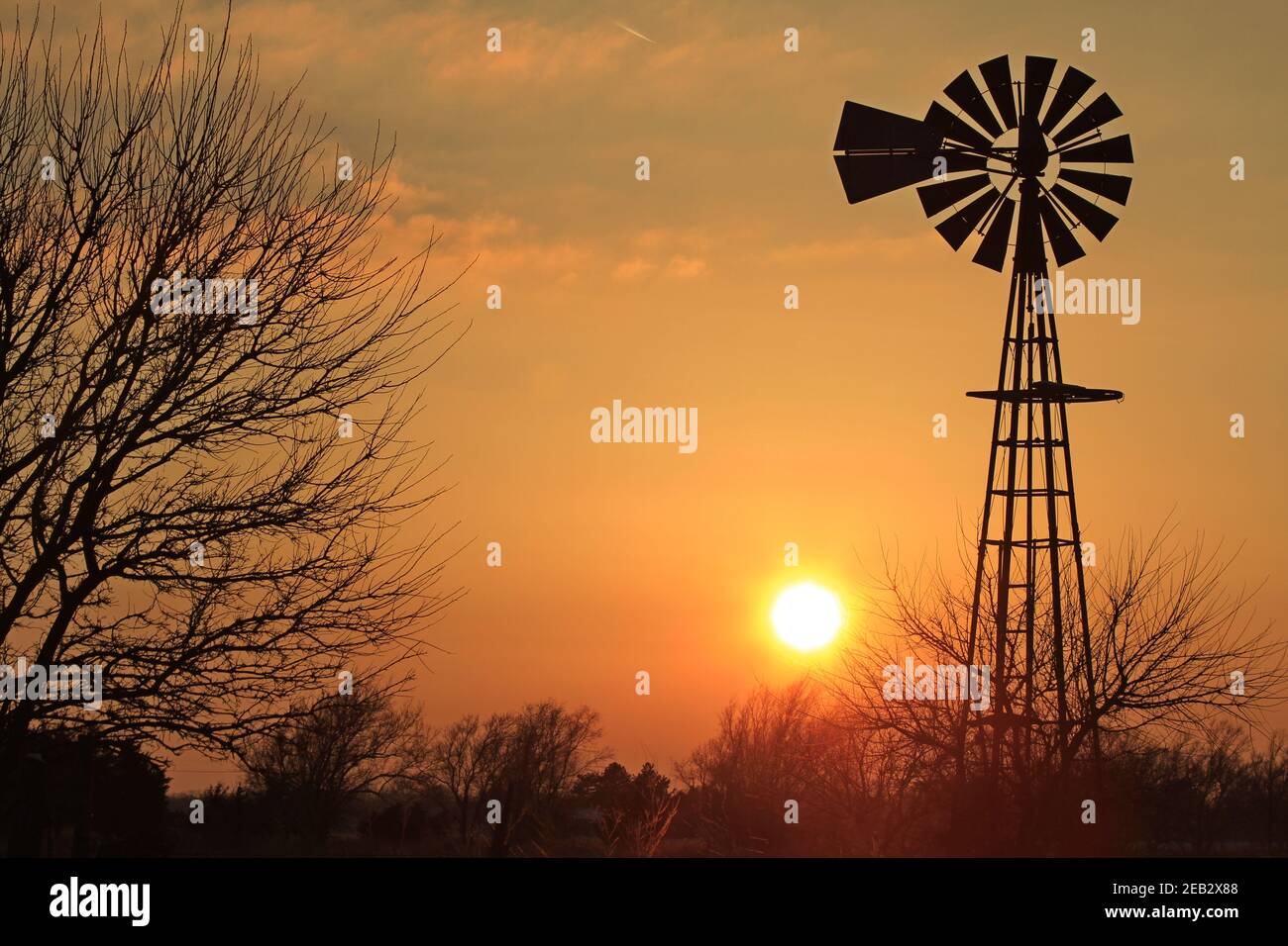 Kansas Sunset con un cielo colorato e nuvole con un mulino a vento e silhouette di alberi è fuori nel paese che è luminoso. Foto Stock