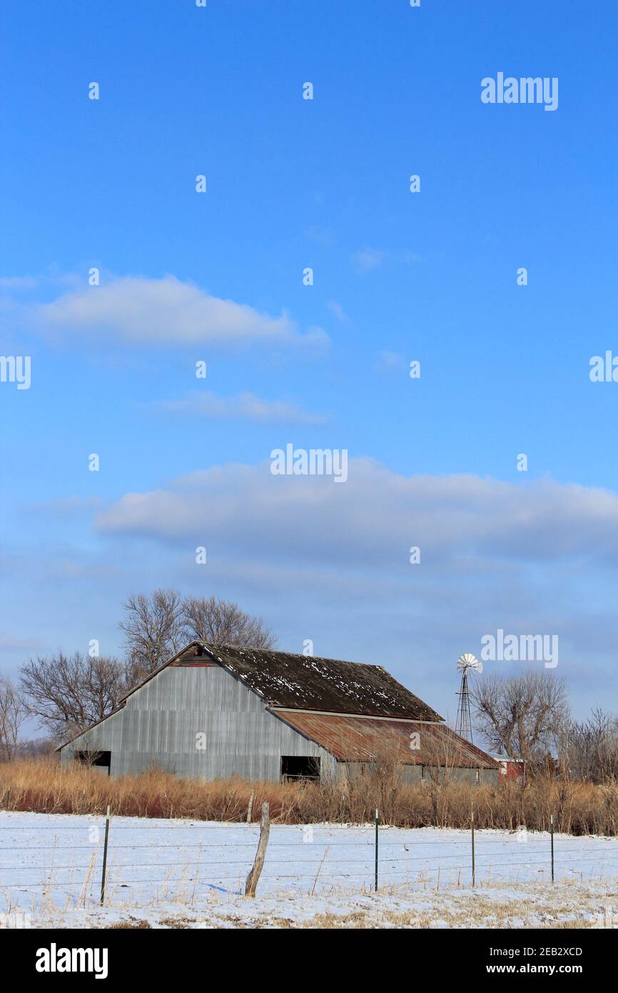 Kansas Country Barn con neve, recinzione, cielo blu e nuvole nel paese che è luminoso e colorato. Foto Stock