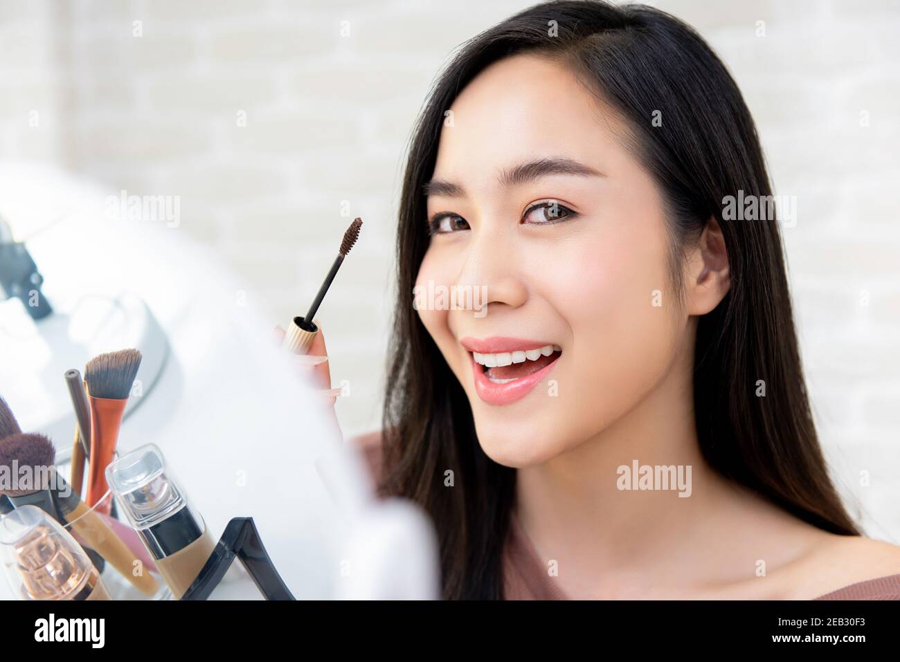 Giovane bella donna asiatica sorridente usando il trucco mascara per le ciglia Foto Stock