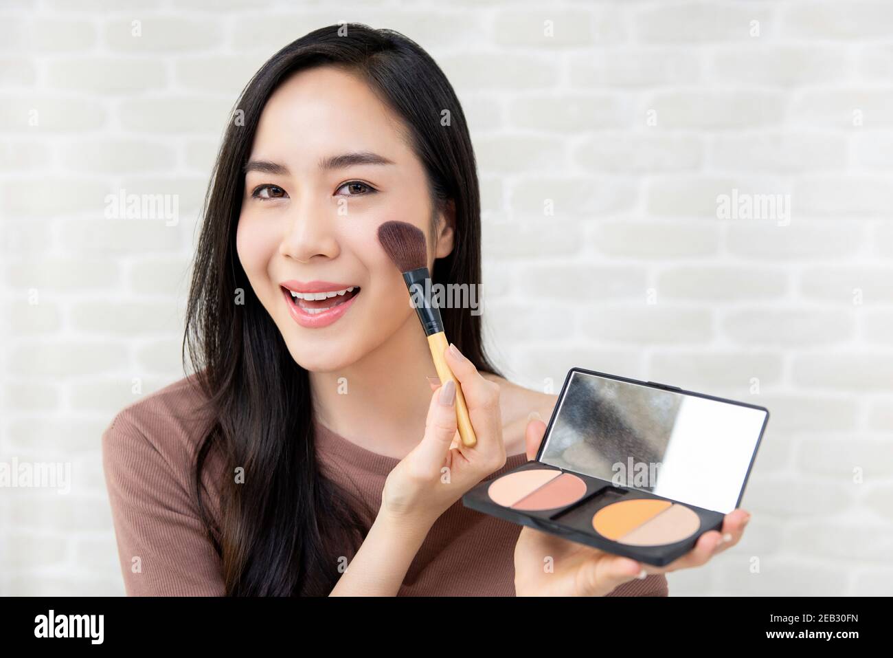 Giovane bella donna asiatica sorridente applicando trucco arrossito su di lei guancia Foto Stock