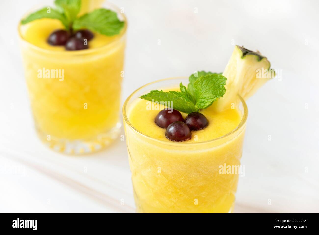 Bevande rinfrescanti sane frullato di frutta di ananas guarnite con le bacche sopra piano di appoggio in marmo bianco Foto Stock