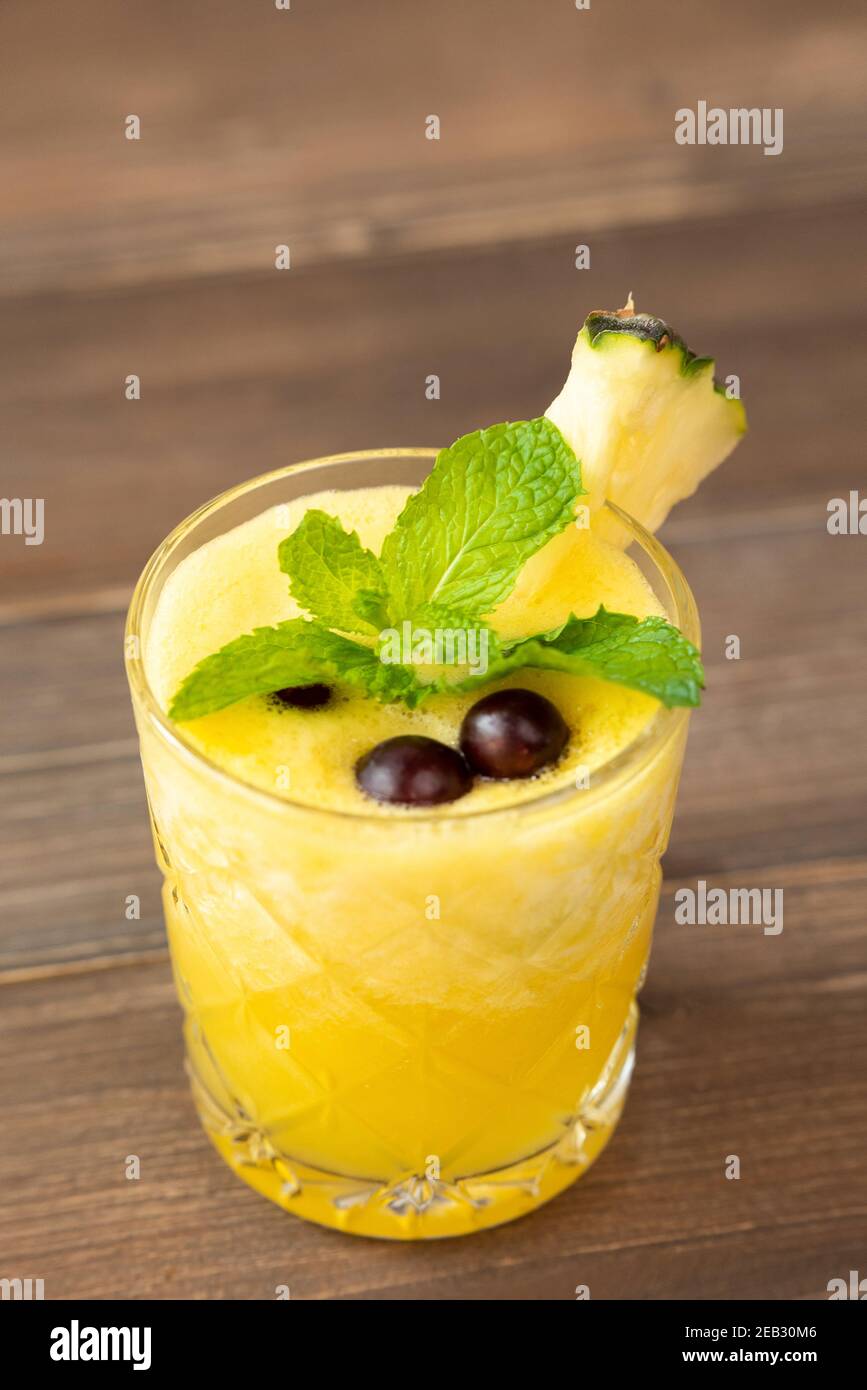 Rinfrescante sano frullato di frutta di ananas bevanda guarnita con bacche sopra tavolo in legno Foto Stock
