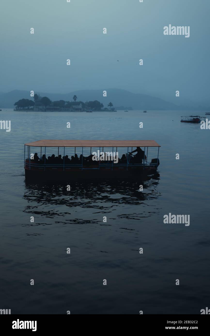 Una barca arancione con sagome di persone su una moodia lago mistico Foto Stock