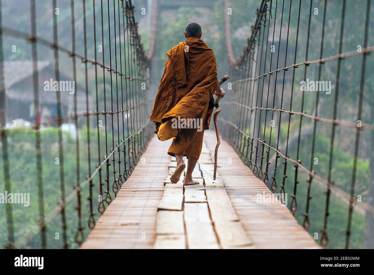 Un monaco con una passeggiata bastone a piedi su un ponte sospeso in legno in un piccolo villaggio di Mae Hong Son, Thailandia. Foto Stock