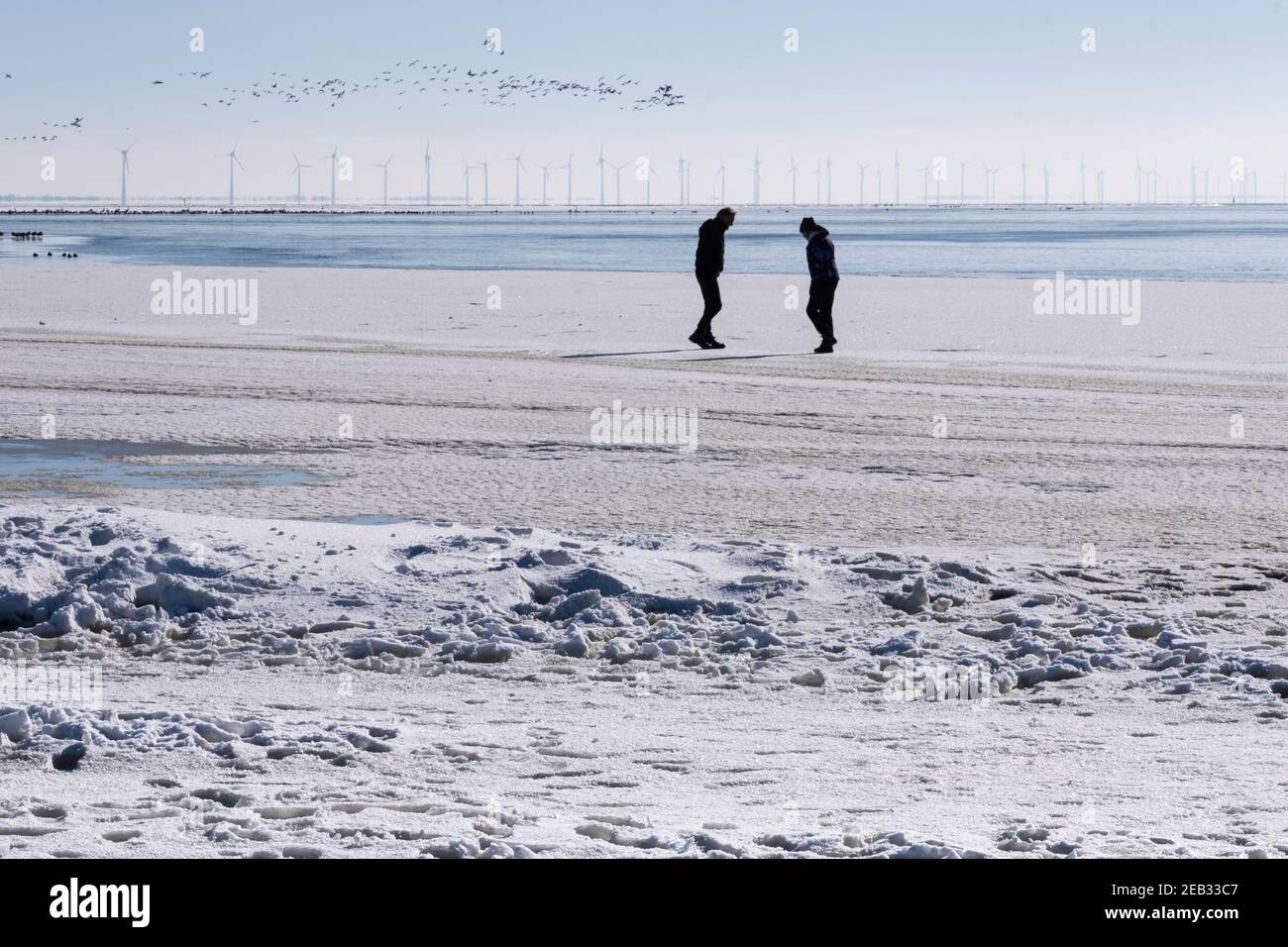 Silhouette di uomo e donna su una spiaggia a Mirns, Paesi Bassi. In background mulini a vento per la generazione di energia sostenibile Foto Stock