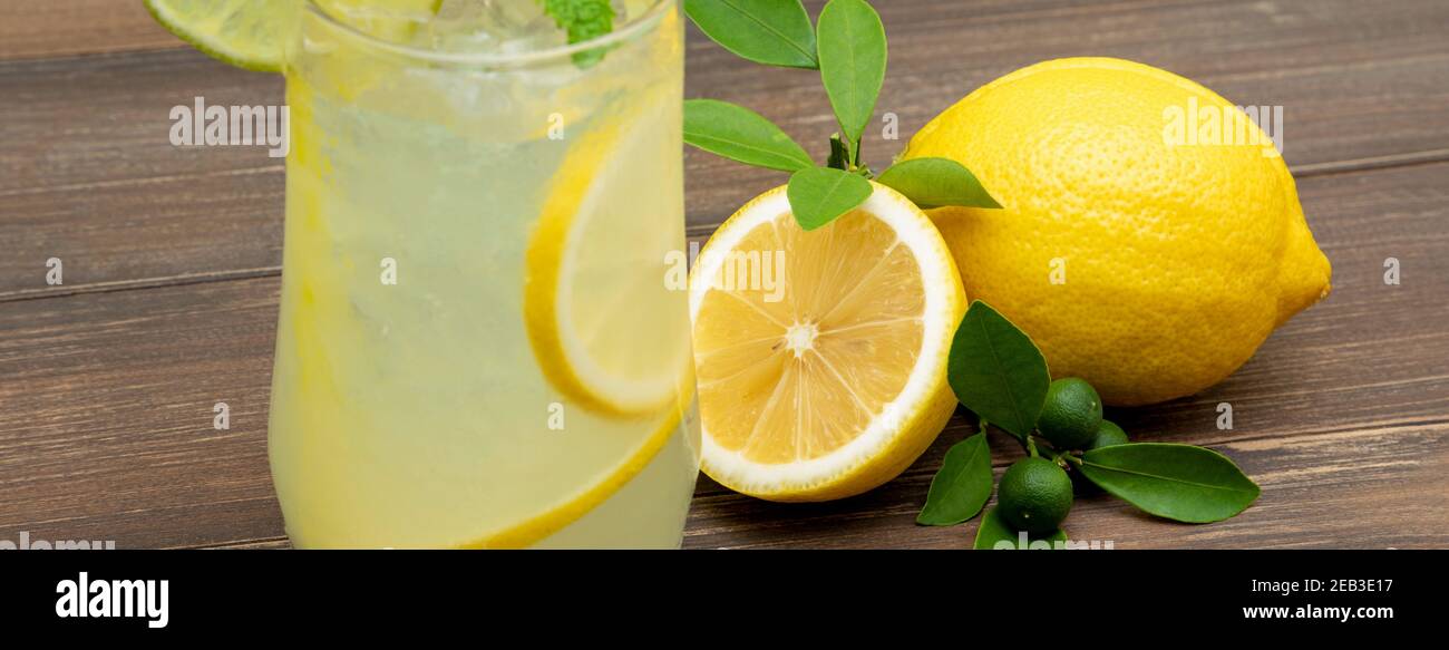 Rinfrescante succo di limonata bevanda nel bicchiere con limoni su sfondo tavola di legno, dimensione banner Foto Stock