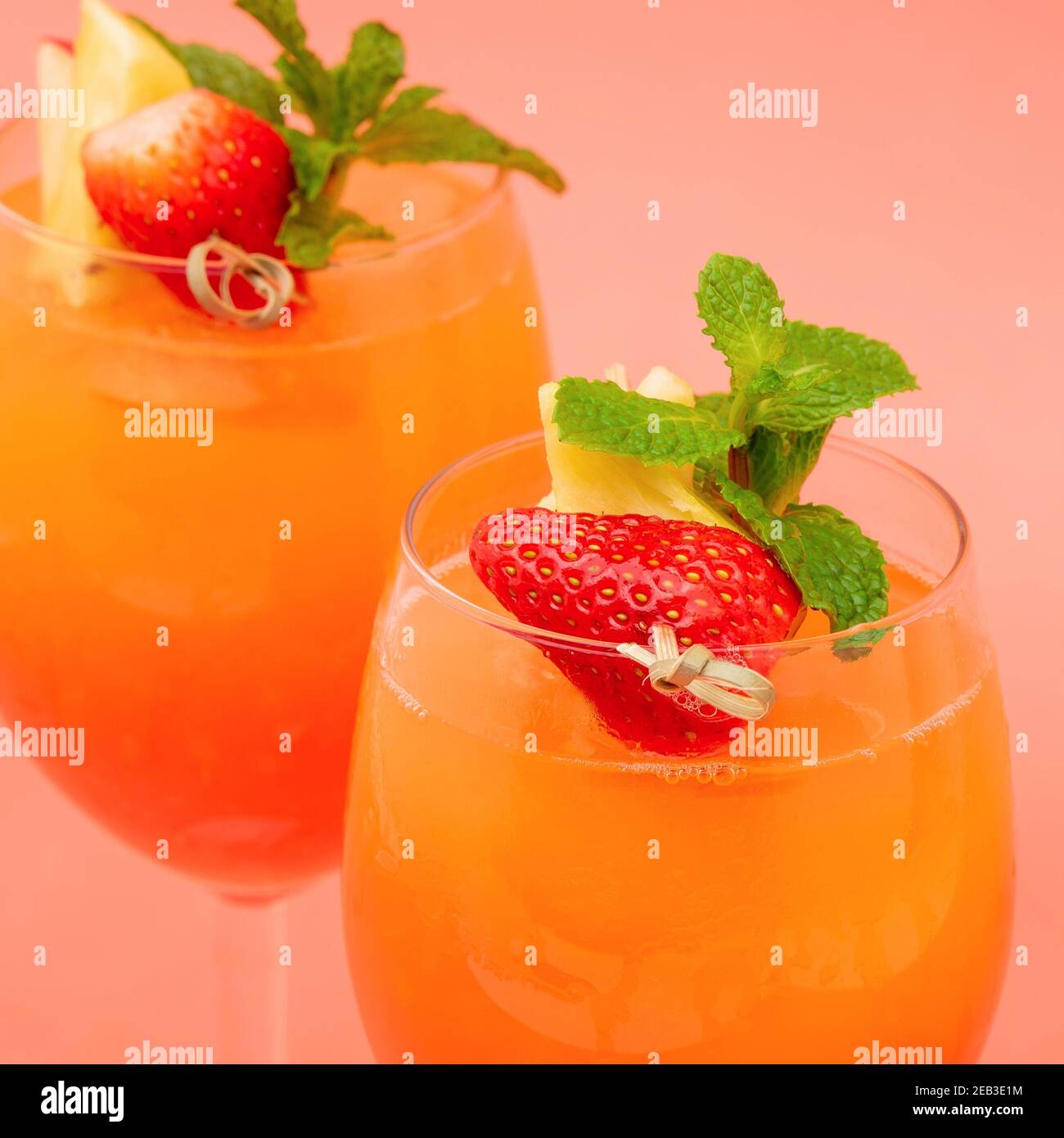 Primo piano di colorati e rinfrescanti cocktail all'alba con fragole e arancio negli occhiali su sfondo rosa corallo Foto Stock
