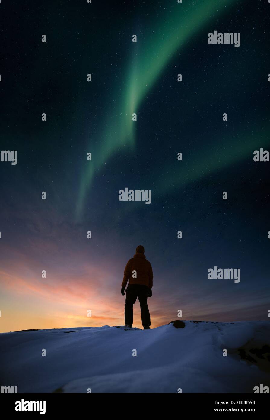 Una persona in piedi su roccia nevosa in inverno e guardando al tramonto e aurora borealis Foto Stock