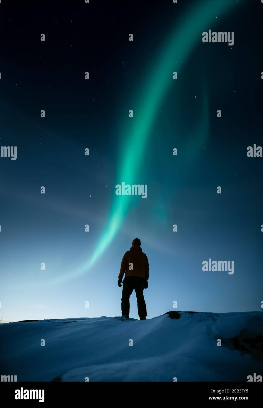 Una persona in piedi su una roccia nevosa in inverno e. guardando l'aurora boreale nel cielo Foto Stock