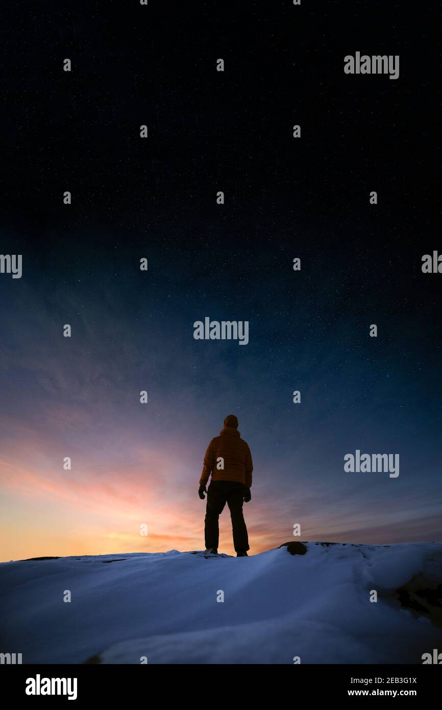 Vista ad angolo basso di un uomo che guarda al tramonto in inverno con le stelle sul cielo Foto Stock