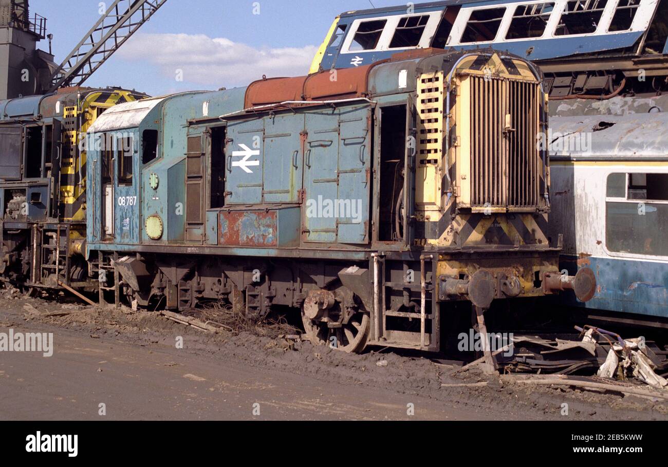 British Rail classe 08 shunter 08787 in fase di demolizione per rottami con altri locomotori shunting e carrozze ferroviarie in background. Foto Stock