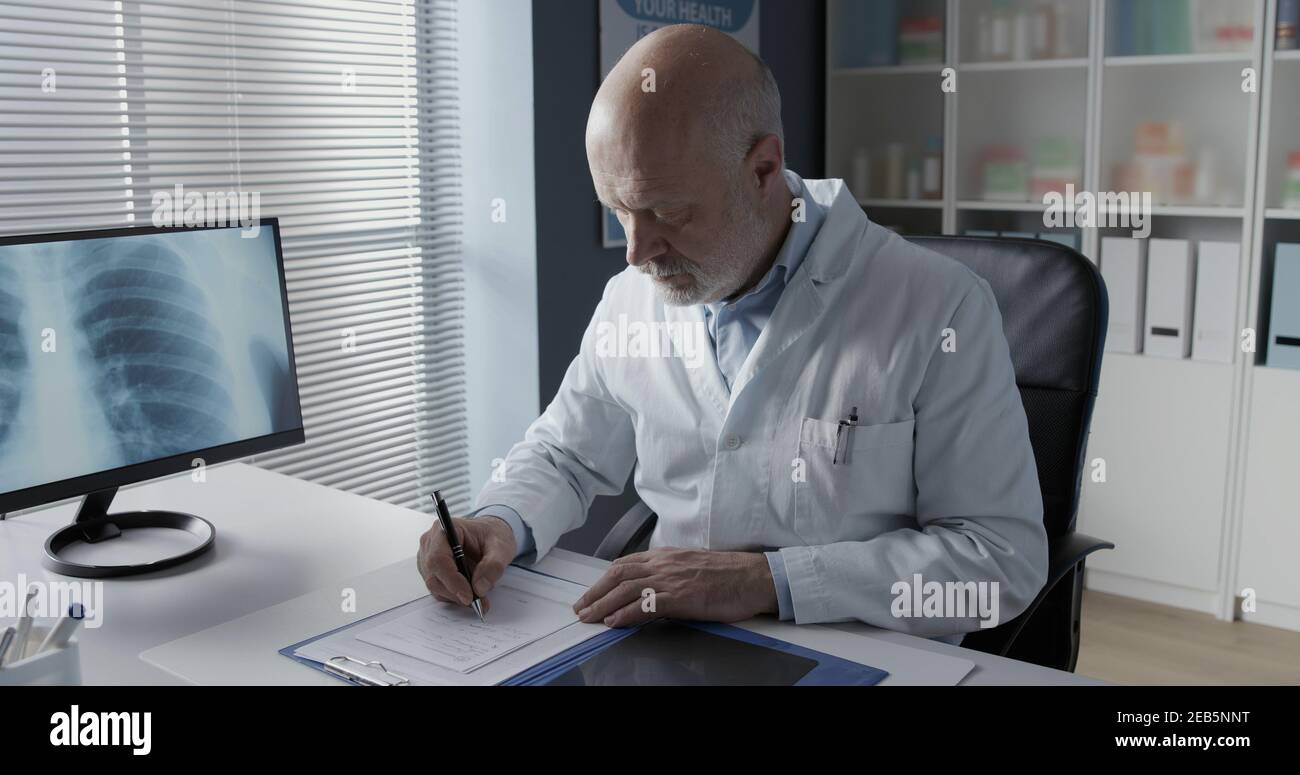 Medico professionista seduto alla scrivania e scrivendo una prescrizione medica per un paziente Foto Stock