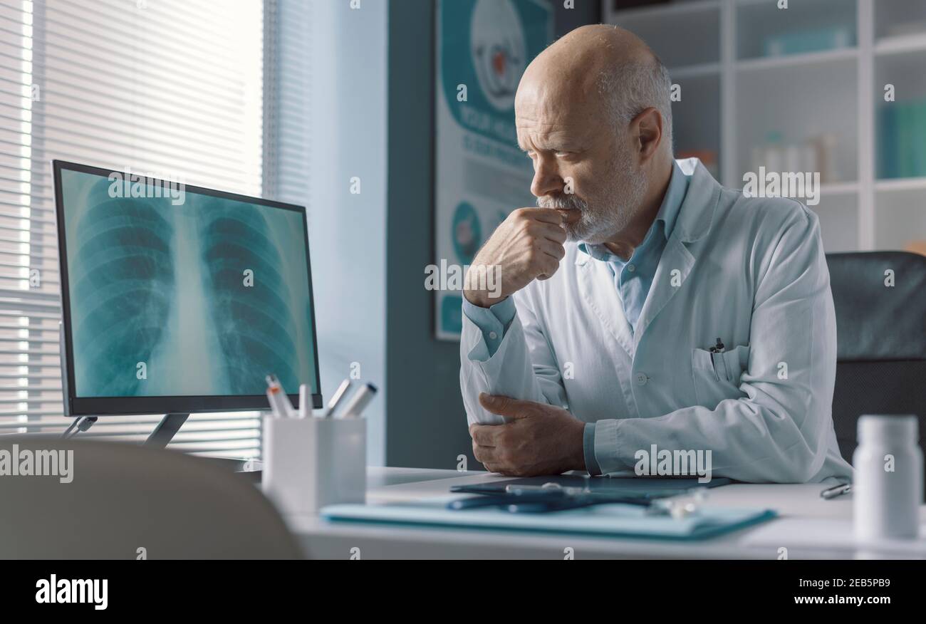 Medico professionista seduto alla scrivania dell'ufficio e che analizza un radiografia immagine sullo schermo del computer Foto Stock
