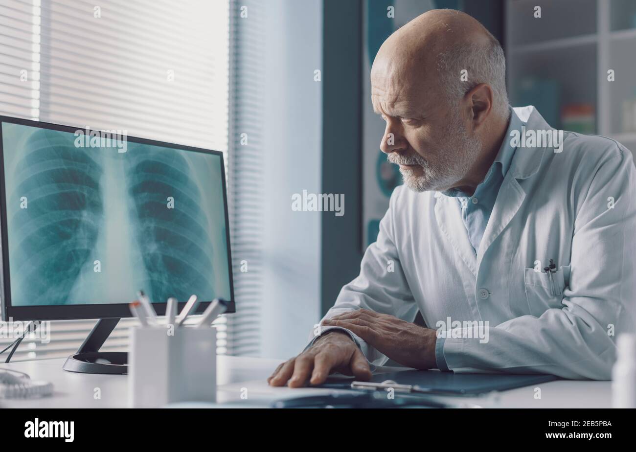 Medico professionista seduto alla scrivania dell'ufficio e che analizza un radiografia immagine sullo schermo del computer Foto Stock