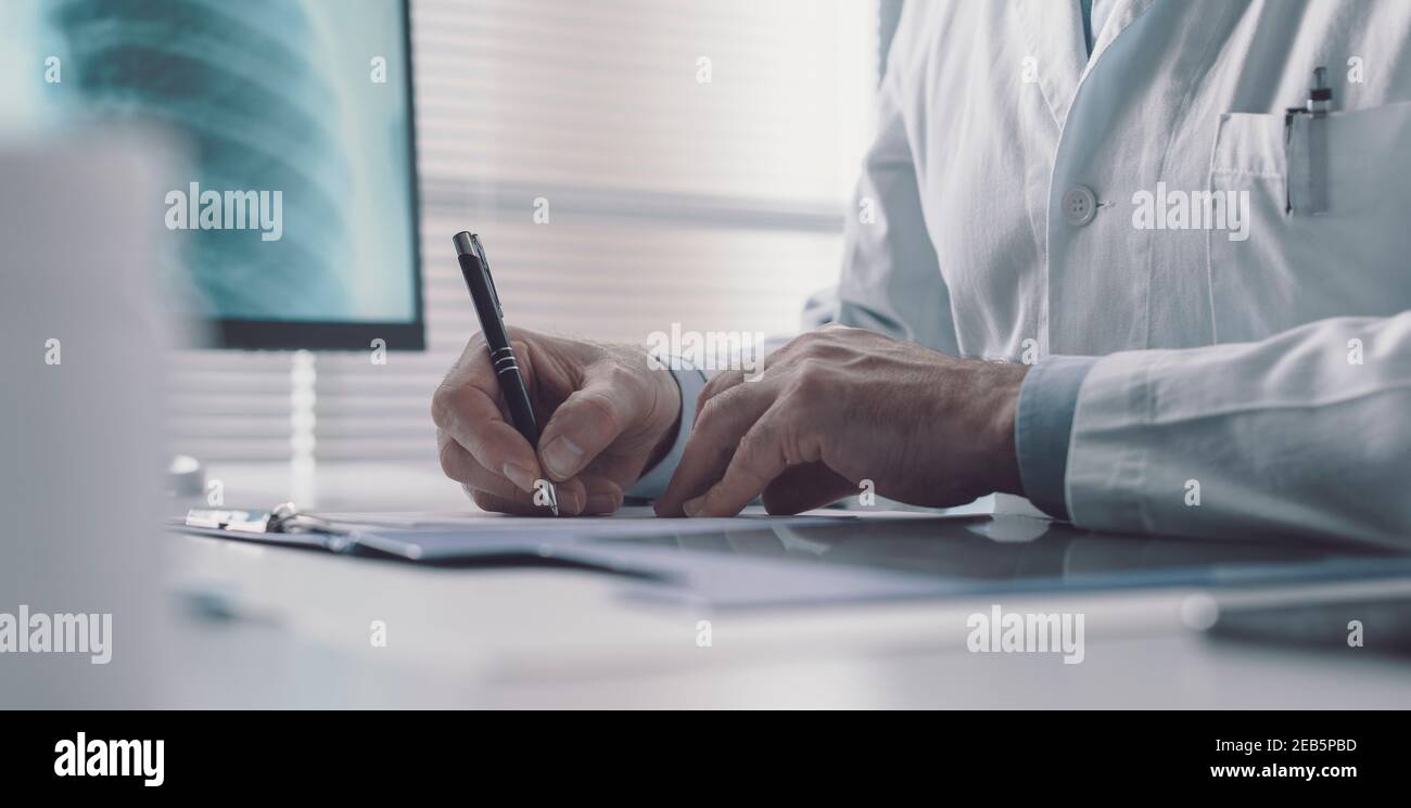 Medico professionista seduto alla scrivania e scrivendo una prescrizione medica per un paziente Foto Stock