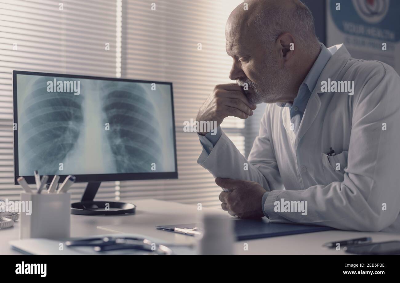 Medico professionista seduto alla scrivania dell'ufficio e che analizza un radiografia immagine sullo schermo del computer Foto Stock