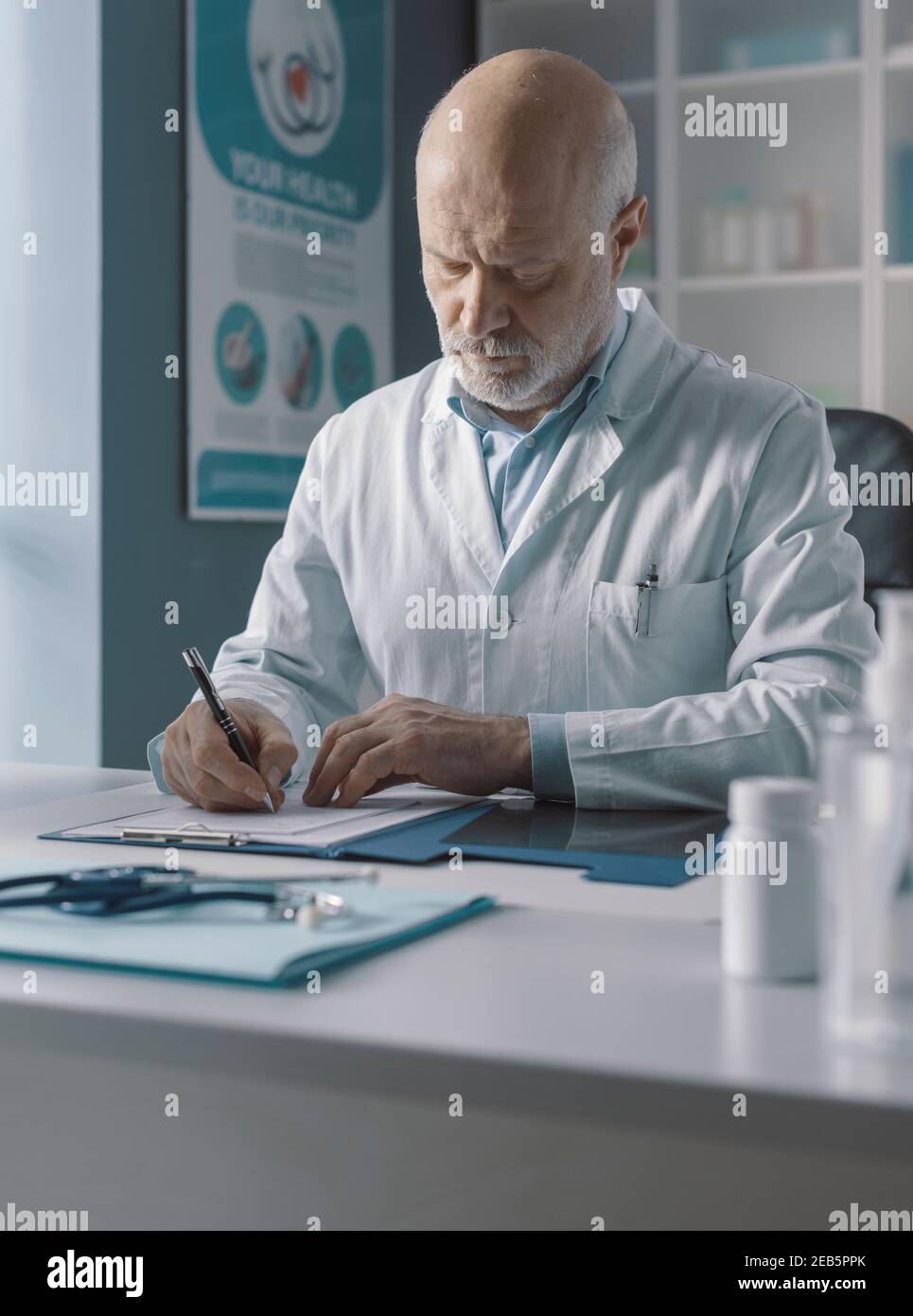 Medico seduto alla scrivania dell'ufficio e scrivendo la prescrizione per il suo paziente Foto Stock