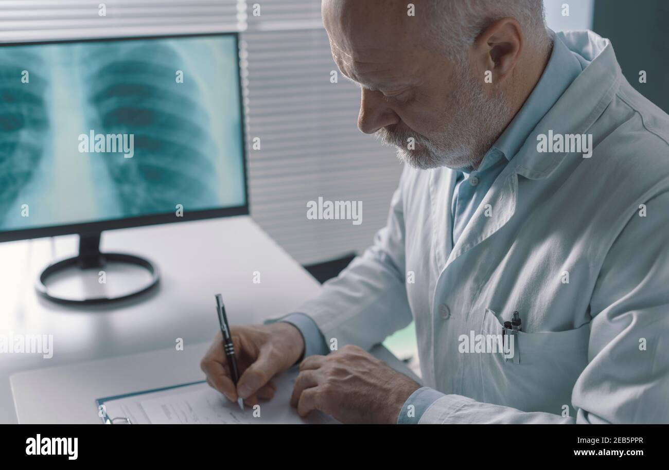 Medico professionista seduto alla scrivania e scrivendo una prescrizione medica per un paziente Foto Stock