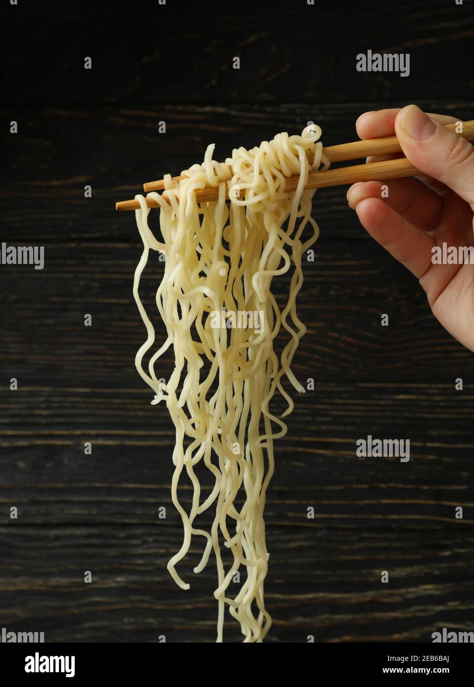 Mano femminile che tiene degli stecchini con noodles istantanei su uno sfondo di legno, concetto di pranzo veloce Foto Stock