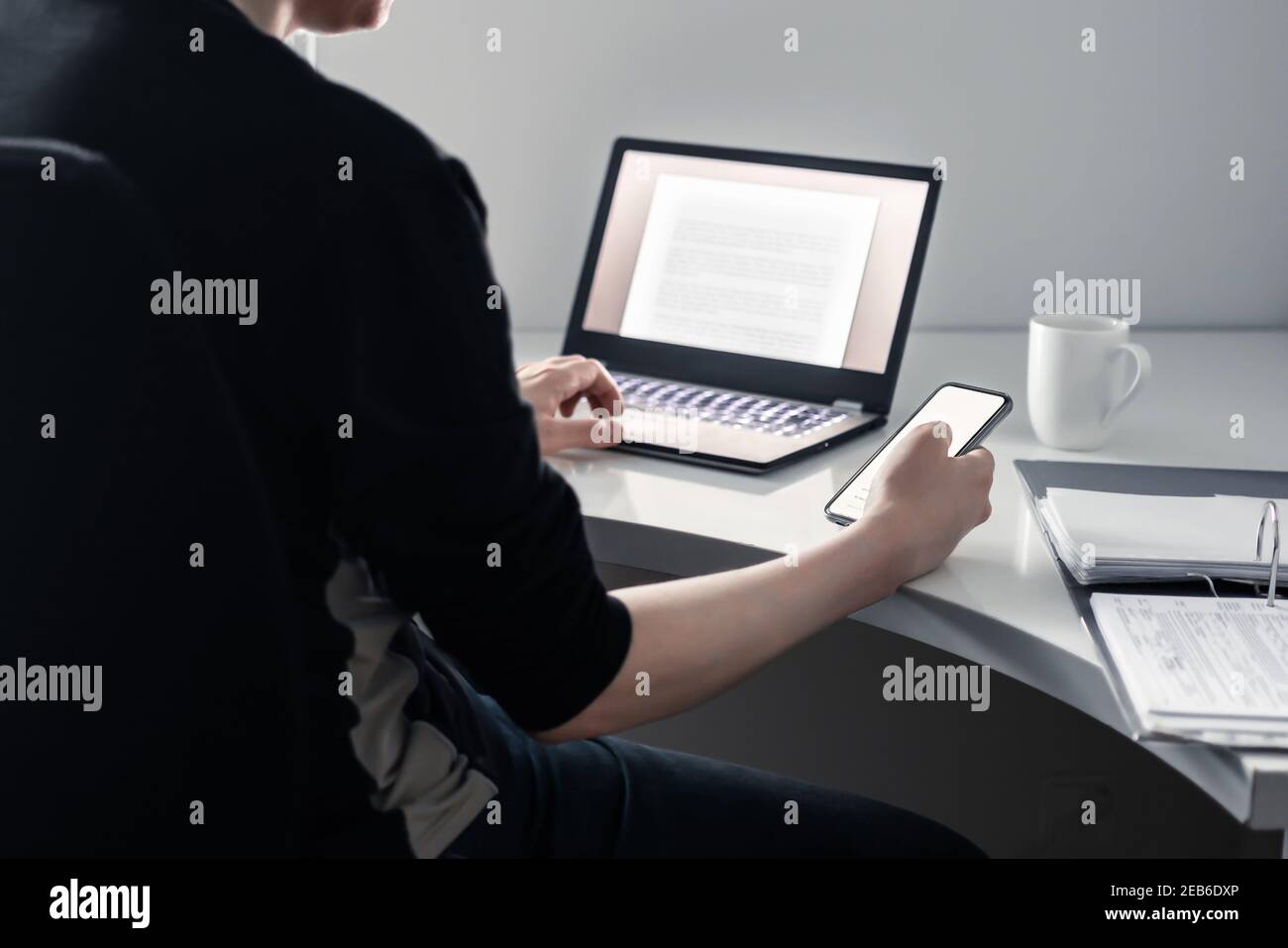 Uomo che usa il telefono e il laptop in ufficio domestico. Applicazione on-line dell'università, assicurazione digitale, prestito o documento ipotecario. Ricerca su Internet con tecnologia. Foto Stock
