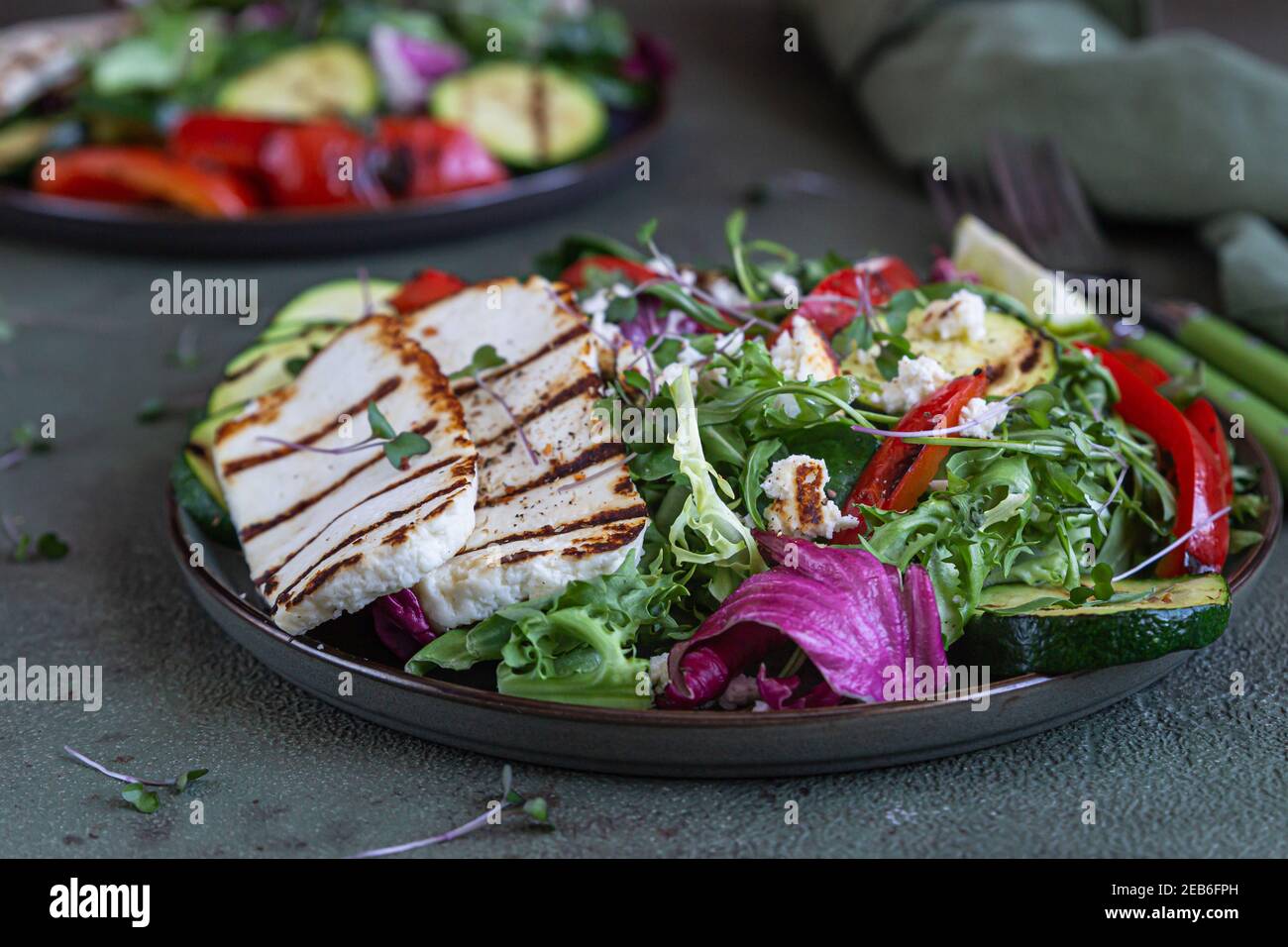 Insalata con formaggio halloumi alla griglia, verdure alla griglia e foglie di insalata mista verde, fondo di cemento verde. Concetto di cibo vegetariano. Messa a fuoco selettiva Foto Stock