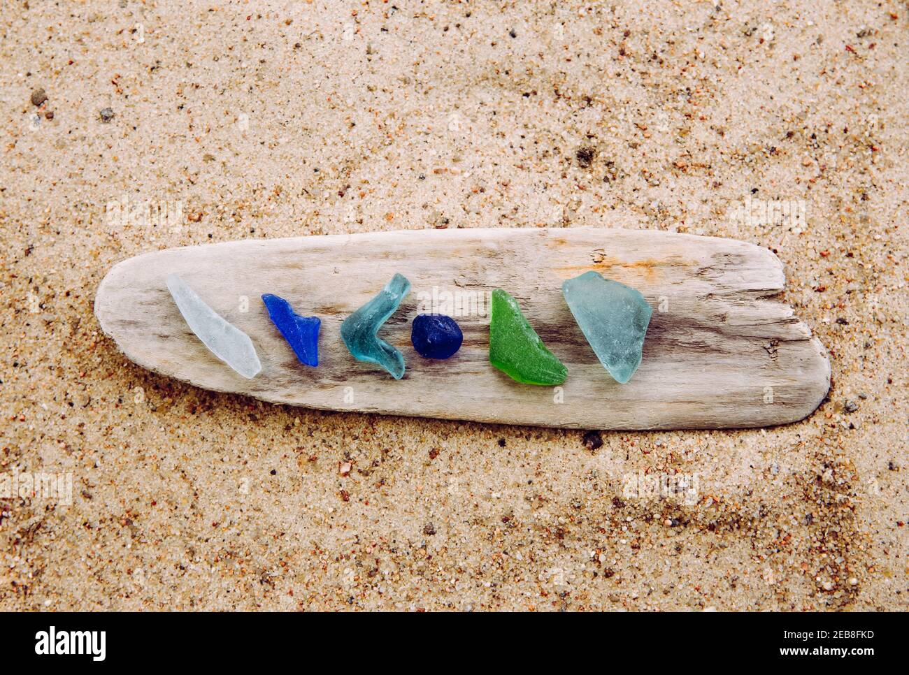 Diverso colore blu, verde, bianco vetro di mare o vetro di spiaggia su driftwood in spiaggia su sabbia. Il vetro è usato per essere pezzi di bottiglia e ora il mare è tumbled. Foto Stock