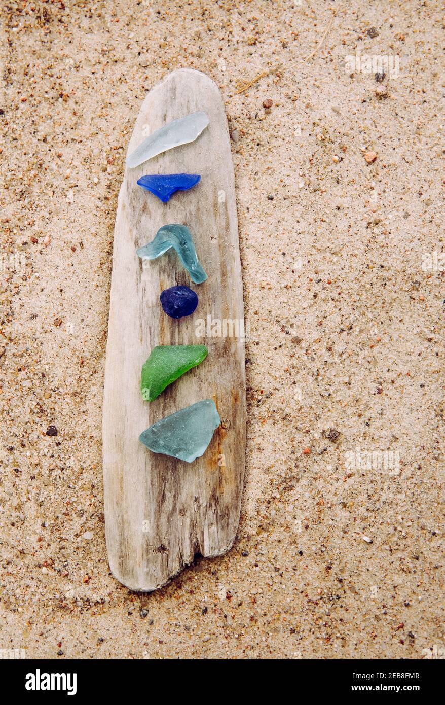 Diverso colore blu, verde, bianco vetro di mare o vetro di spiaggia su driftwood in spiaggia su sabbia. Il vetro è usato per essere pezzi di bottiglia e ora il mare è tumbled. Foto Stock