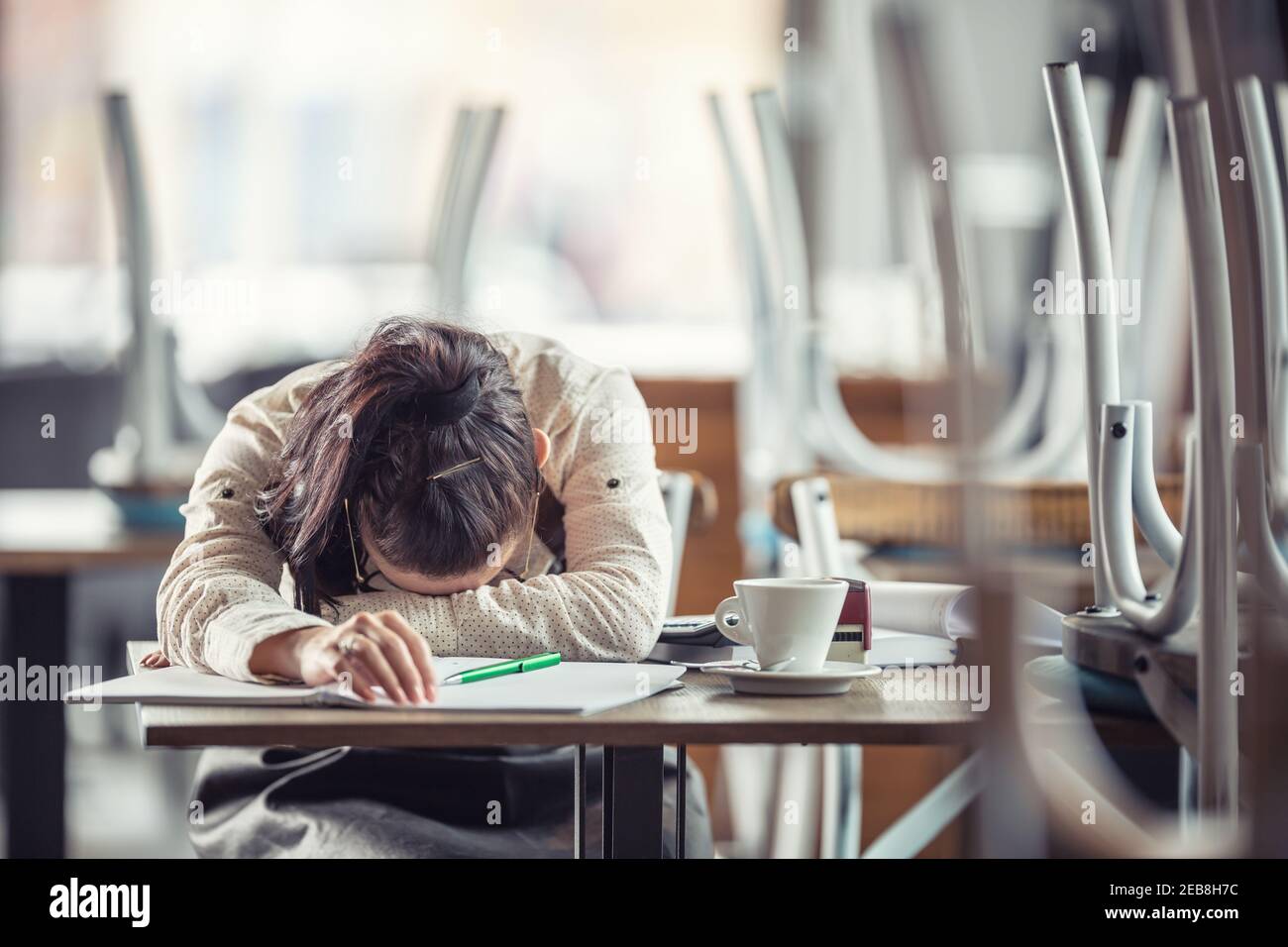Il proprietario di affari femminile esausto appoggia la sua testa sul tavolo dopo mucchi di documenti fatti al bar dopo le ore. Foto Stock