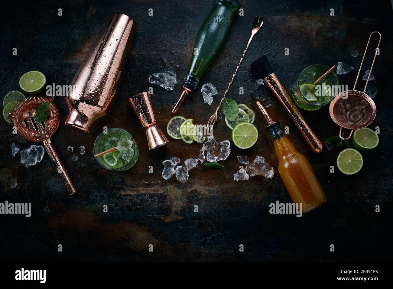 Cocktail e bevande alcoliche di sottofondo con una varietà di sparsi utensili in rame e shaker per cocktail intervallati da cubetti di ghiaccio e. sli fresco Foto Stock