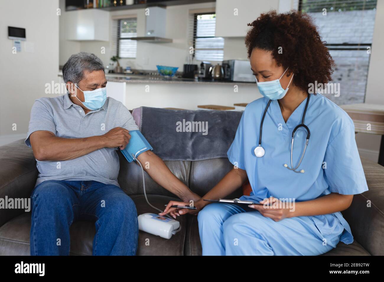 Senior misto uomo di razza con femmina medico a casa che visita indossare maschere facciali che prendono la pressione sanguigna Foto Stock